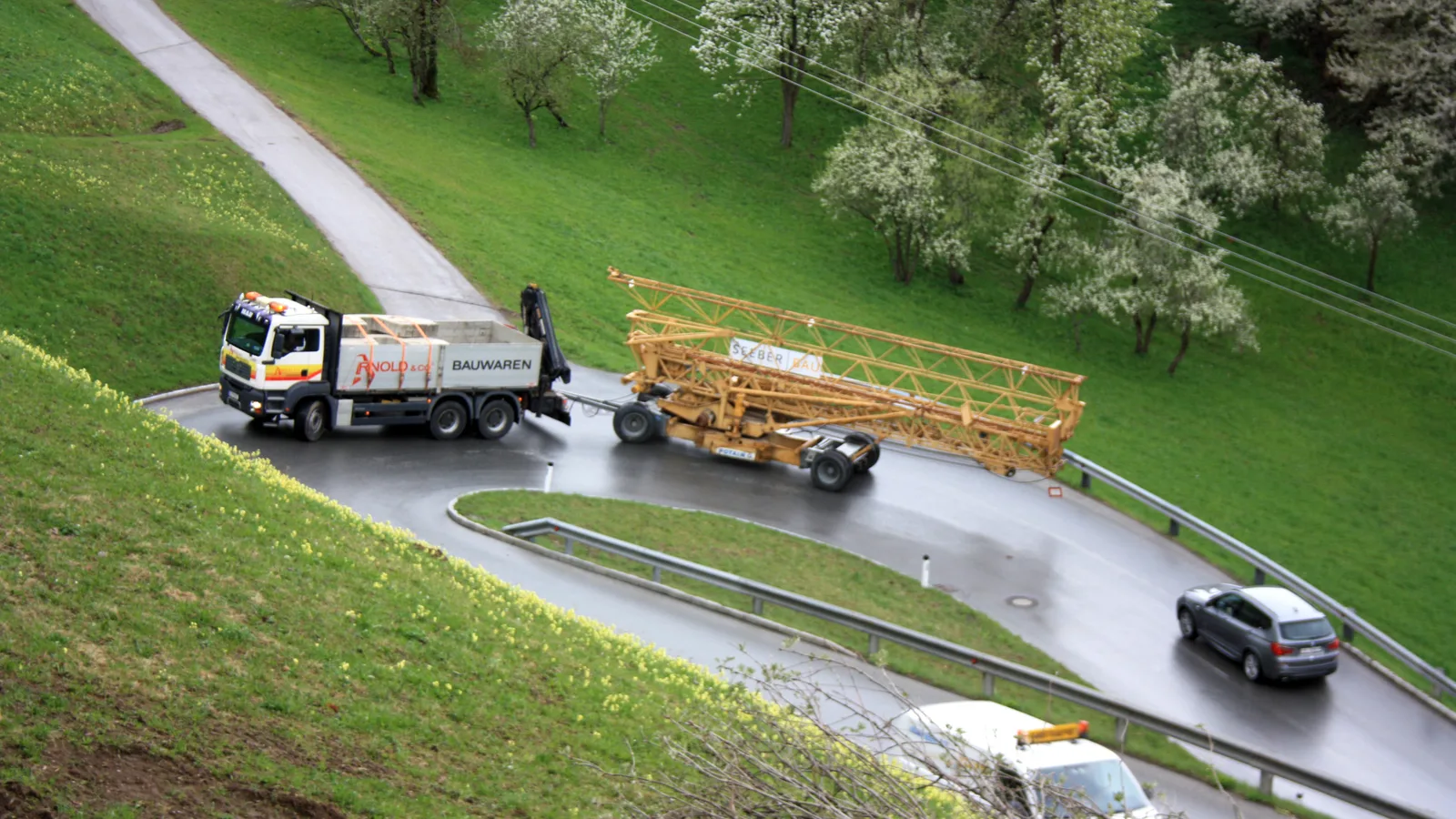 Ein Kranwagen liefert Holz an einer schmalen Straße am Hang, aufgenommen von oben.