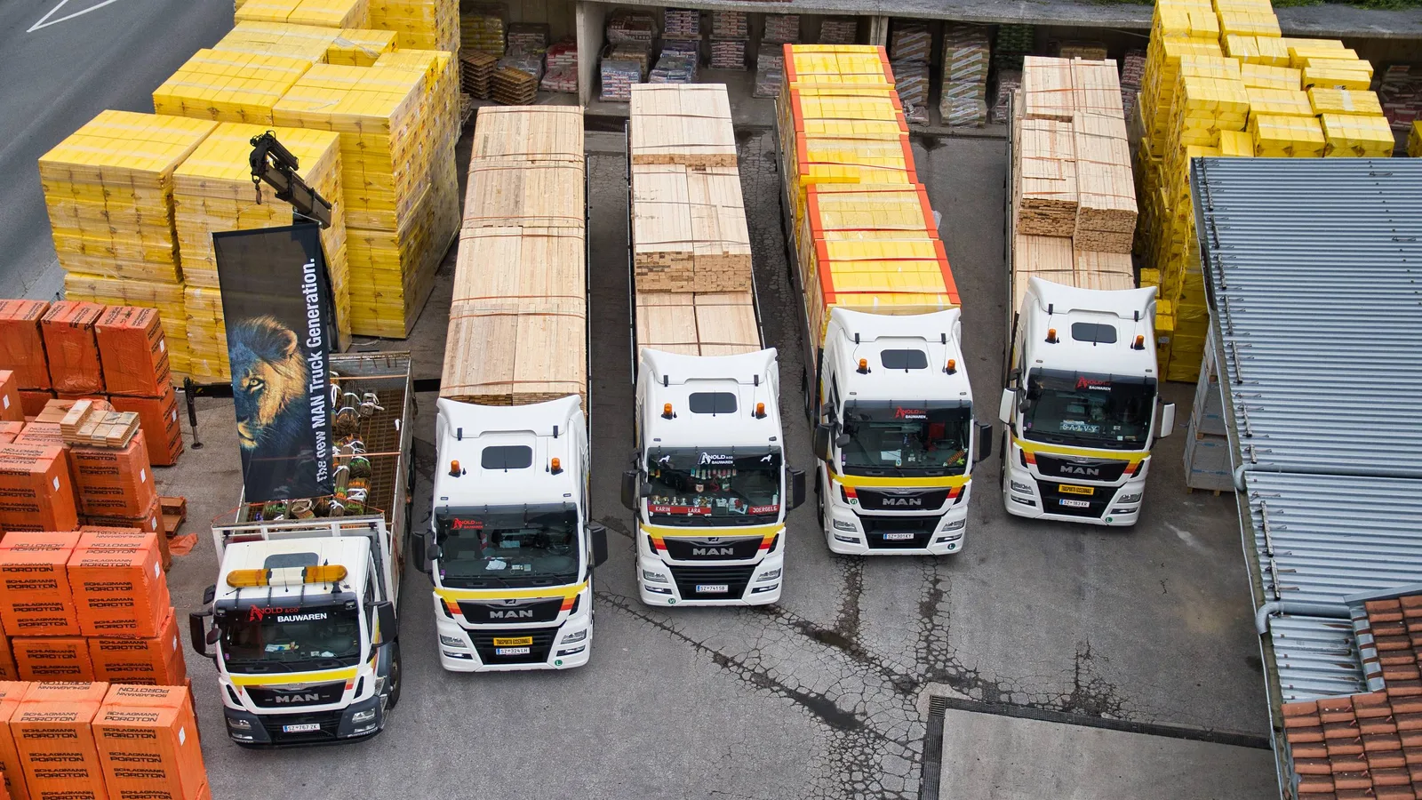 Luftbild des Lagerplatzes mit aufgereihten Lastwagen, Ziegelpaletten und gelb verpackten Dämmstoffen.