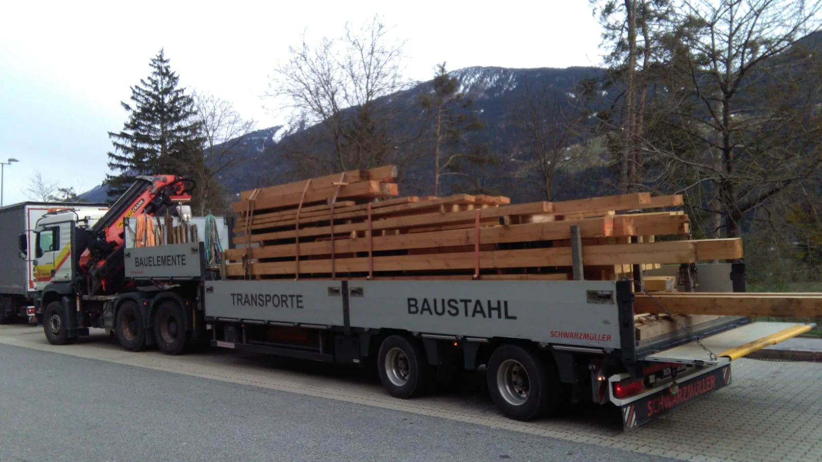 Sattelzug mit langer Holzladung, auf der Plane sind die Wörter Transporte und Baustahl zu lesen.